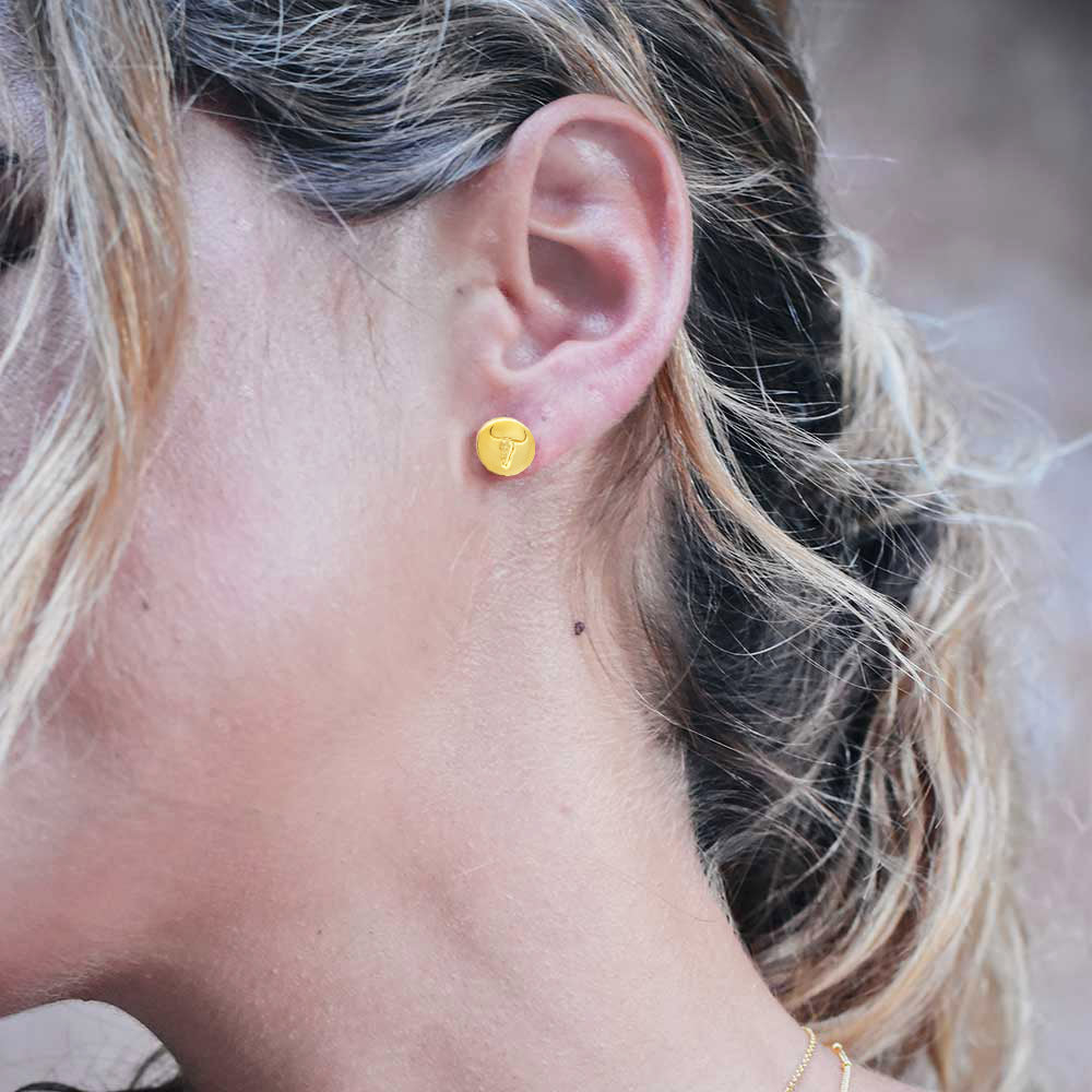 Model wears 18kt gold vermeil coin stud earrings with engraved western style steer head by Azuni